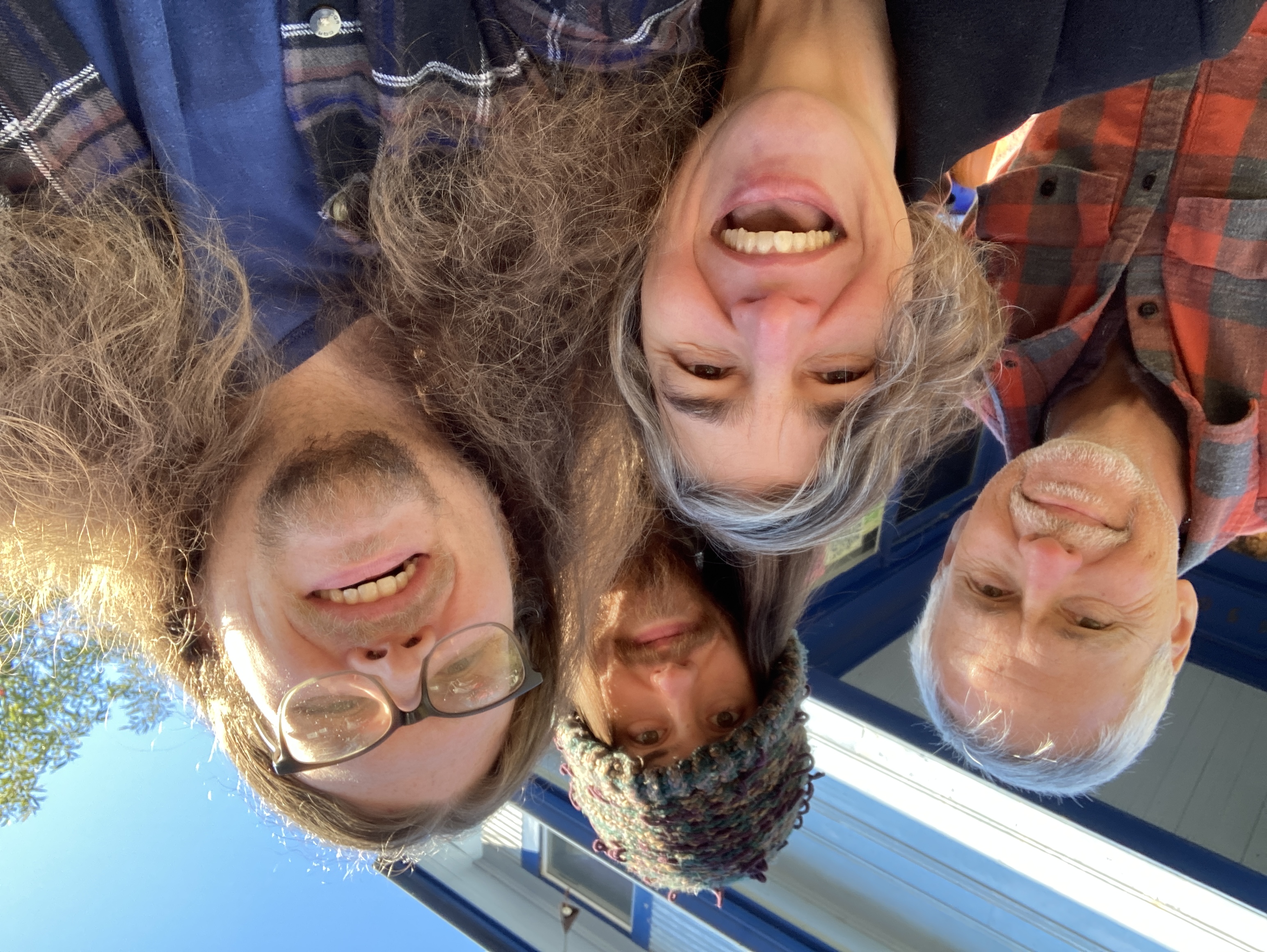 The heads of 4 white people of a variety of ages fill the photo. They're smiling and laughing outside on a sunny day.